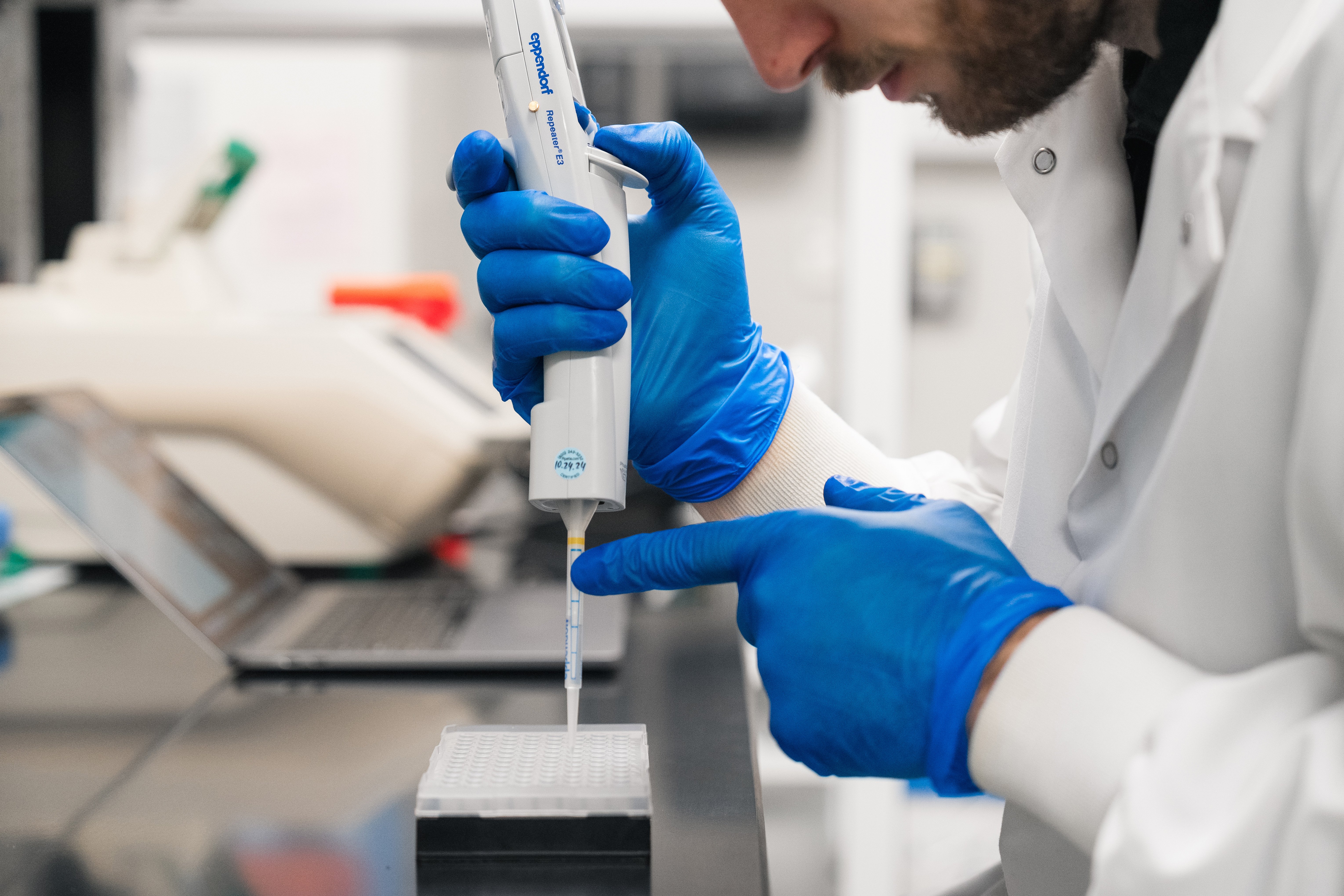 An image of a person in a lab coat pipetting consumables into laboratory tubes